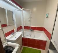 A bathroom in a 3-room apartment with a bathtub, washing machine, and red and white tiles.