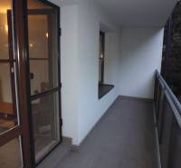 A balcony of a 2-room apartment with a view of the surrounding greenery, access through glass doors.