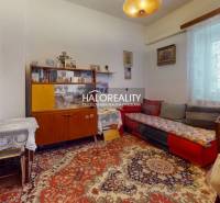A room in a family house with retro furniture, a floral carpet, and lace curtains.