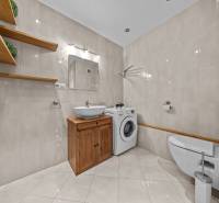 A bathroom in a 3-room apartment with light tiles, wooden shelves, and a washing machine.