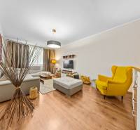 A bright living room in a three-room apartment with wood-patterned flooring and a yellow armchair.