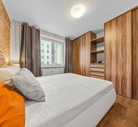 A bedroom in a 3-room apartment with a wooden decor floor and a brick wall.