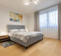 Bedroom in a two-room apartment with a wood-patterned floor and a gray bed.