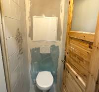 A toilet with wooden doors in a 3-room apartment, incomplete tiles, and a white floor.