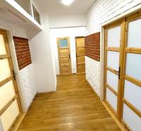 A hallway with brick cladding, wooden doors, and a floor with a wooden design in a 3-room apartment.