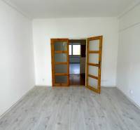 A room in a 3-room apartment with a wooden decor floor, white walls, glass doors.