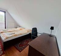 A bedroom with a bed, table, and carpet in a 3-room apartment with a wooden decor floor.