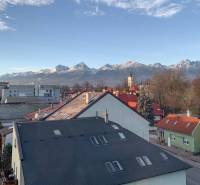 View of the High Tatras from Poprad over the rooftops of houses, snow-covered mountains in the distance.