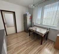 A kitchen in a 3-room apartment with a wooden decor floor, a dining table, and appliances.