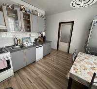 A kitchen in a 3-room apartment with a wood-patterned floor, modern appliances, and a dining table.