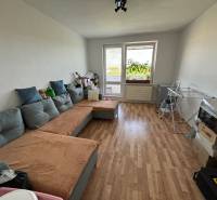 Living room with a sofa and wood-patterned flooring in a three-room apartment.