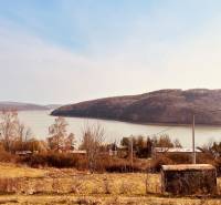 View of recreational plots in Nová Kelča near the water and wooded hills.