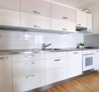 A kitchen in a 2-room apartment with a white kitchen unit and a floor with a wood decor.