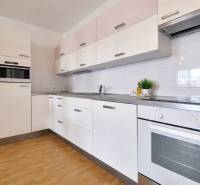 A kitchen unit in a 2-room apartment with a wooden decor floor and white cabinets.