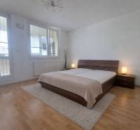 A bedroom with large windows, a double bed, and a wooden decor floor in a 2-room apartment.