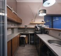 A kitchenette in a commercial space with a coffee machine, wooden cabinets, and a floor with a wooden decor.