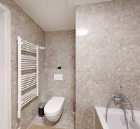 A bathroom in a studio apartment with a bathtub and a wall radiator on grey tiles.