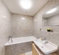 A bathroom with a bathtub and a sink lined with stone tiles in a studio apartment.