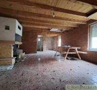Interior of a cabin with brick walls, a wooden ceiling, and a bench seat.