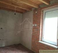 A room in a cottage with a brick wall, wooden ceiling, and a window with a blind.