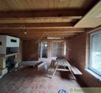 Interior of a cabin with wooden decor, seating area with a table and a fireplace on a brick wall.