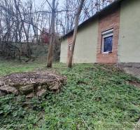 A cottage in Chľaba surrounded by trees, with a stone detail in the foreground.