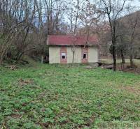 A cottage in Chľaba surrounded by greenery and forest, with a small bridge leading across the meadow.