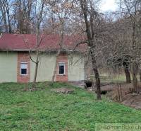 A cottage in Chľaba with trees, greenery, and hilly terrain in the surroundings.