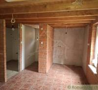 Interior of a cabin with brick walls, wood-patterned flooring, and ceiling beams.