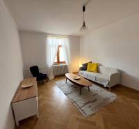 Living room of a two-room apartment with a wooden decor floor, a light sofa, and decorative pillows.