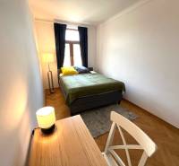 Bedroom in a 2-room apartment with a bed, a desk, and a wooden decor floor.
