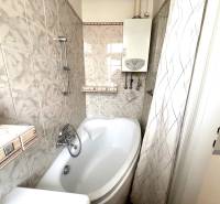 A bathroom in a 2-room apartment with a bathtub and a gas boiler, tiles in light tones.