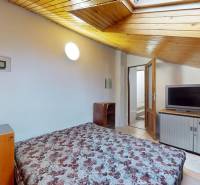 Attic bedroom of a 3-room apartment with a TV, built-in safe, and wooden ceiling.