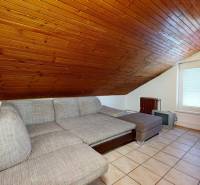 The image shows an attic room with a sofa and a slanted wooden ceiling.