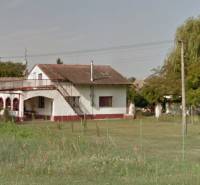 A family house in Kúty with a veranda, a garden, and surrounded by trees and grass.
