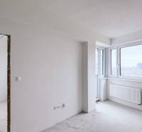A bright room with large windows in a 3-room apartment without floor coverings.