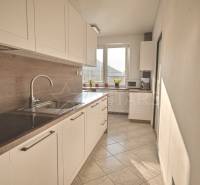 A kitchen with light cabinets and a wood-patterned floor in a three-room apartment.
