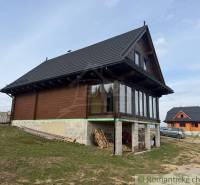 The family house in Lom nad Rimavicou is wooden with a black roof and large windows.