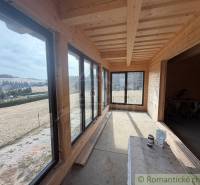Interior of a family house with wood-patterned flooring and large windows, surrounding fields.