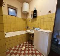 A bathroom in a family house with a bathtub, sink, and washing machine, yellow tiles on the walls.