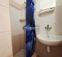 A bathroom in a studio apartment with a sink, shower, and blue curtain.