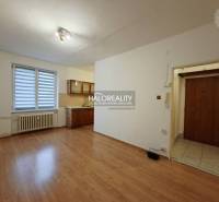 A studio apartment with a wooden floor, a kitchenette, and an entrance door.