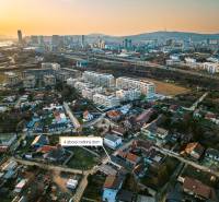 An aerial view of a neighborhood with family houses and the panorama of Bratislava at sunset.