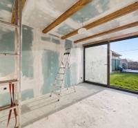 The interior of a family house with a ladder, raw walls, and glass doors to the garden.