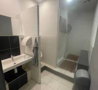 Bathroom in commercial premises with a sink, shower, and light-colored tiles.
