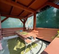 A wooden gazebo by the cottage in Martin with benches and a table, protected by a screen.
