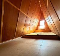 Attic of a cottage with a mattress and a window, wooden interior.