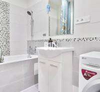 Bathroom in a 2-room apartment with a washing machine, a bathtub, and a floral-patterned curtain.