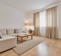 A living room of a family house with a beige sofa, a coffee table, and a wooden-patterned floor.