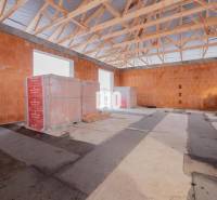 An unfinished interior of a family house with brick walls and a wooden ceiling frame.